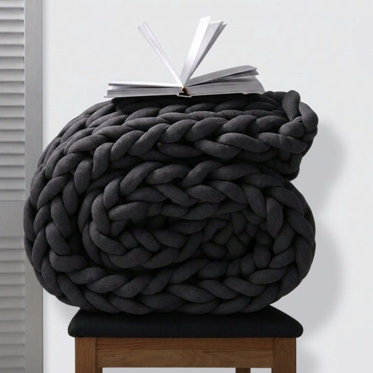 BloomKnit chunky cotton knitted weighted blanket in Midnight Ash, folded on a wooden stool | midnight-ash