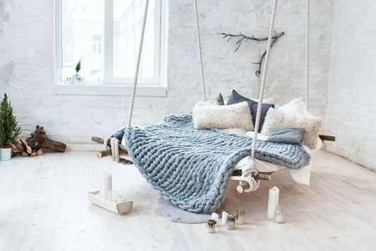 Chunky knit weighted blanket on cozy swing bed with pillows and candles, creating a calming sleep environment.