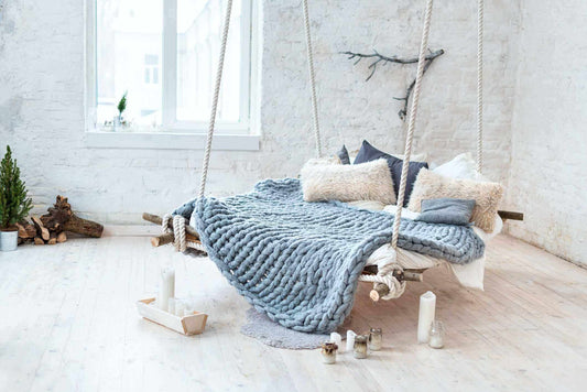 Chunky knit weighted blanket on cozy swing bed with pillows and candles, creating a calming sleep environment.