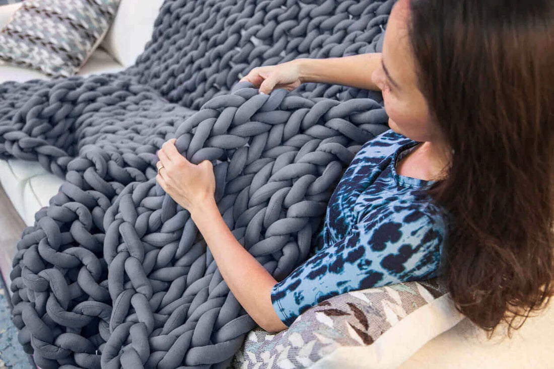 woman sitting on a bed wrapped in a chunky knit weighted blanket