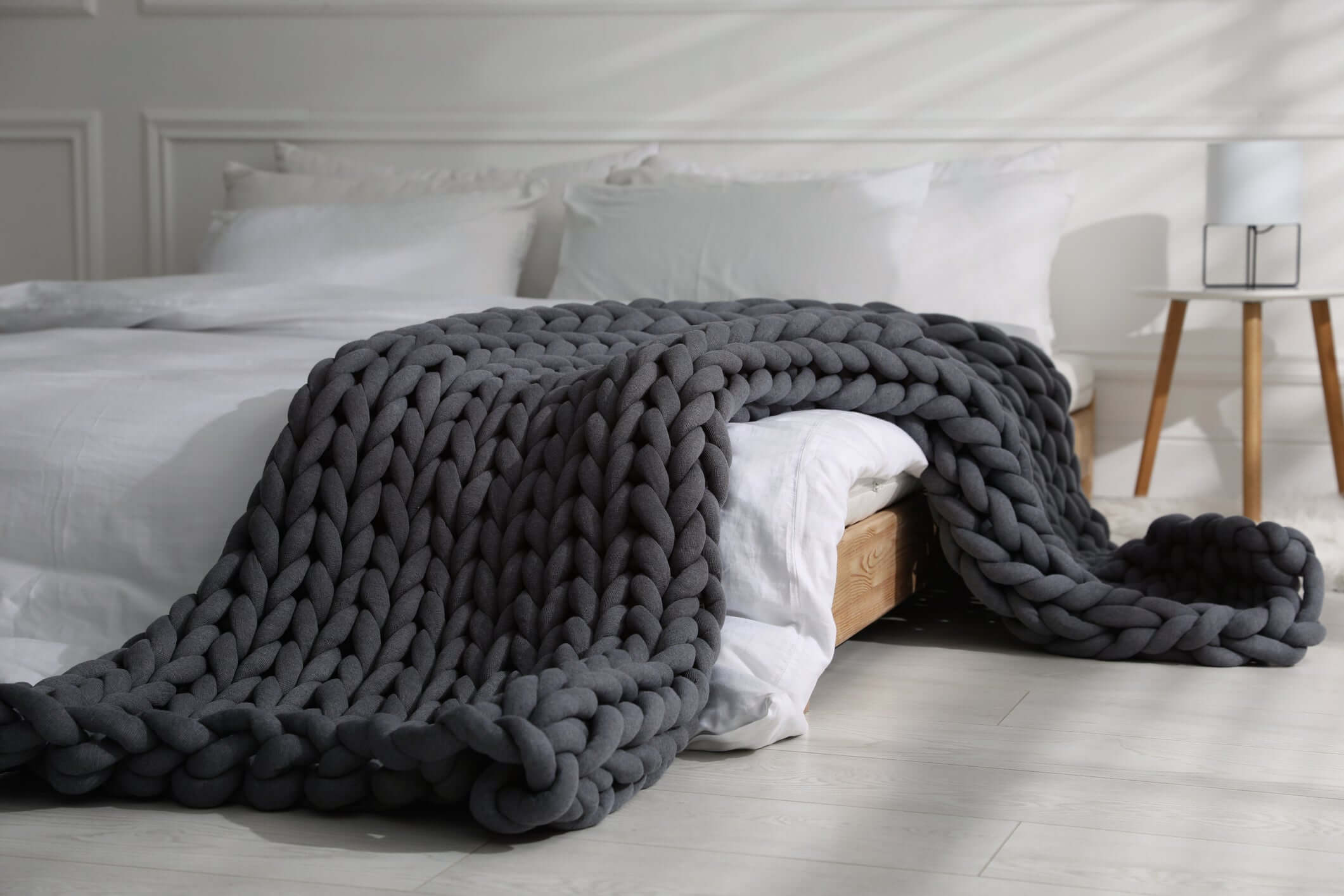 BloomKnit chunky cotton weighted blanket in Midnight Ash draped over a bed in a bedroom setting
