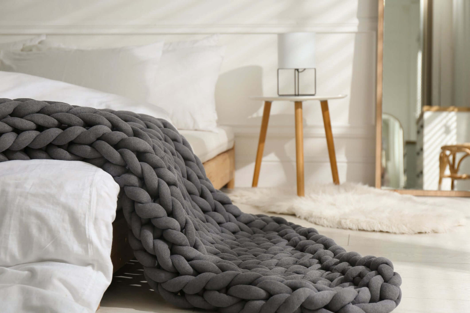 Midnight Ash BloomKnit chunky cotton weighted blanket draped over a white bed in a bright bedroom