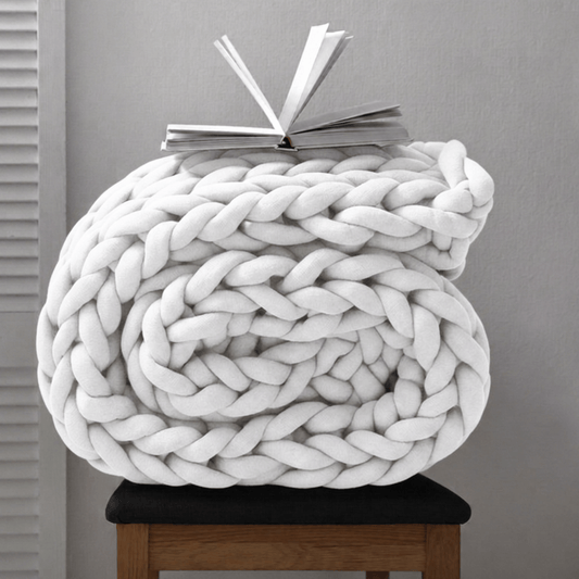 BloomKnit chunky cotton knitted weighted blanket in pure white folded on a wooden stool | pure white