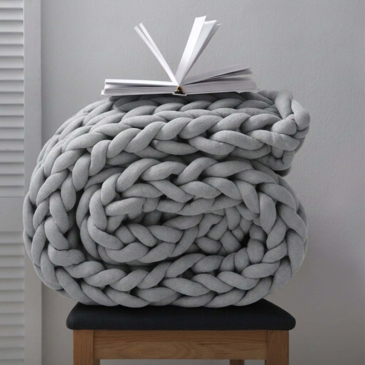 BloomKnit chunky cotton knitted weighted blanket in cloudstone, folded on a wooden stool | cloudstone