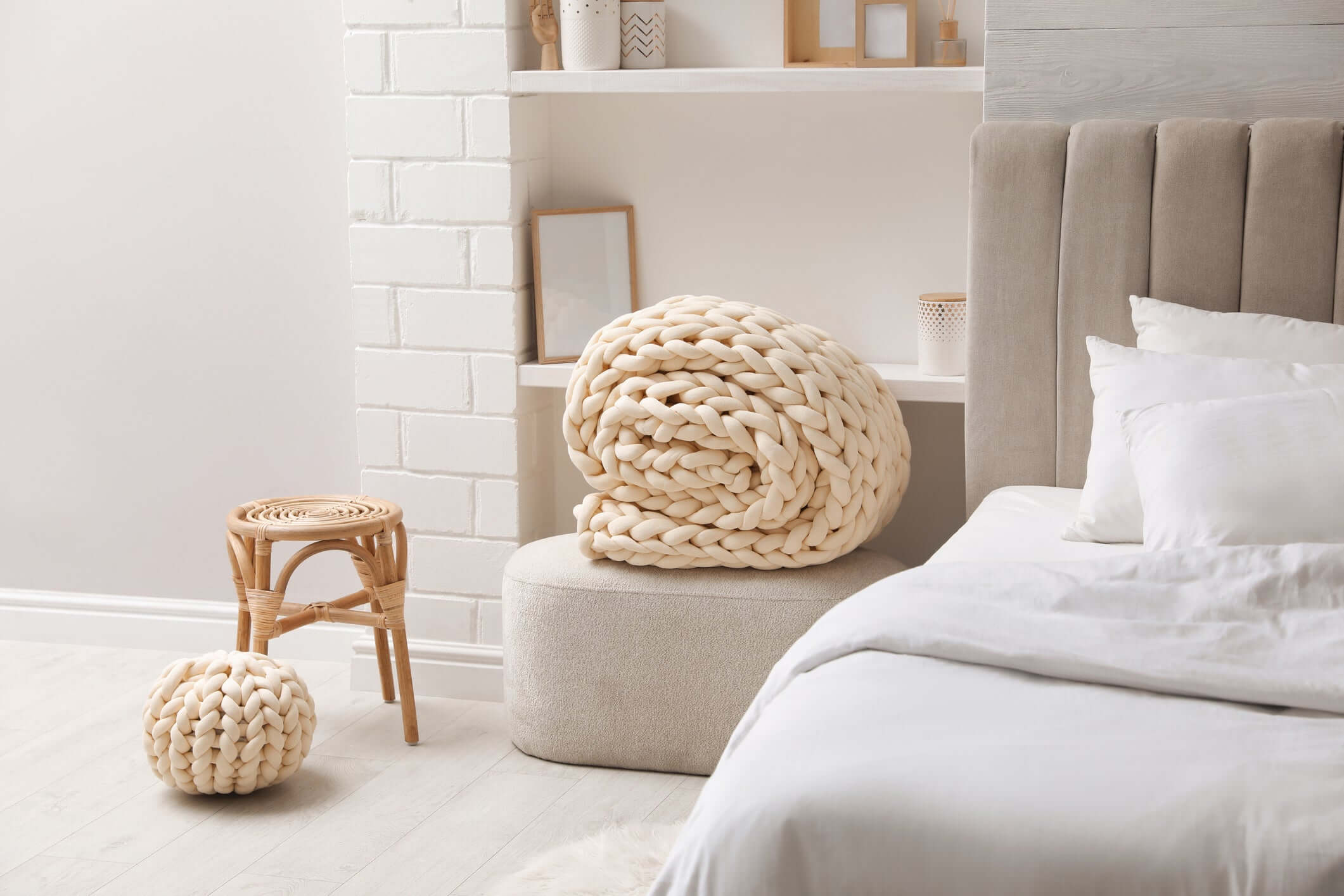 Chunky cotton knit weighted blanket in warm sand in a cozy minimalist bedroom with a taupe headboard, small stool, and natural decor.